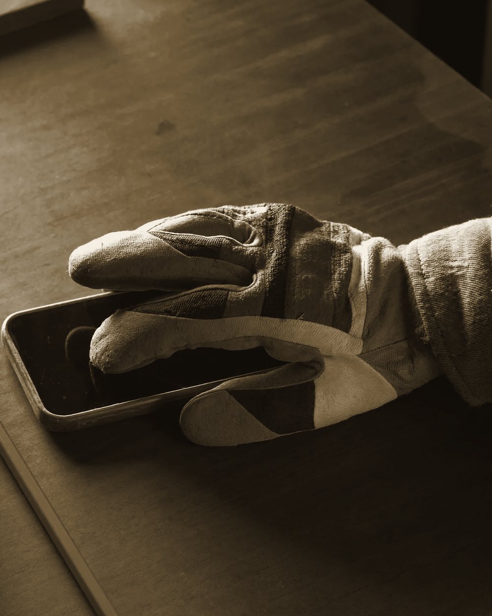 Hand im Arbeitshandschuh tippt auf ein Smartphone auf der Werkbank